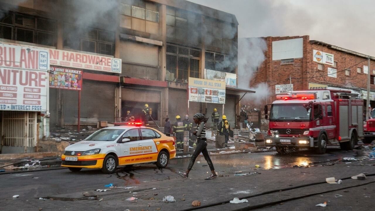 Une femme marche près d'un camion de pompiers en intervention après une nouvelle nuit de violences, à Johannesburg, en Afrique du Sud, le 12 juillet 2021. © Yeshiel Panchia, AP Photo