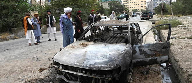 Des Taliban se trouvent à côté d'une voiture détruite par un tir de roquettes, à Kaboul, le 30 août 2021. © Wakil Kohsar, AFP Text
